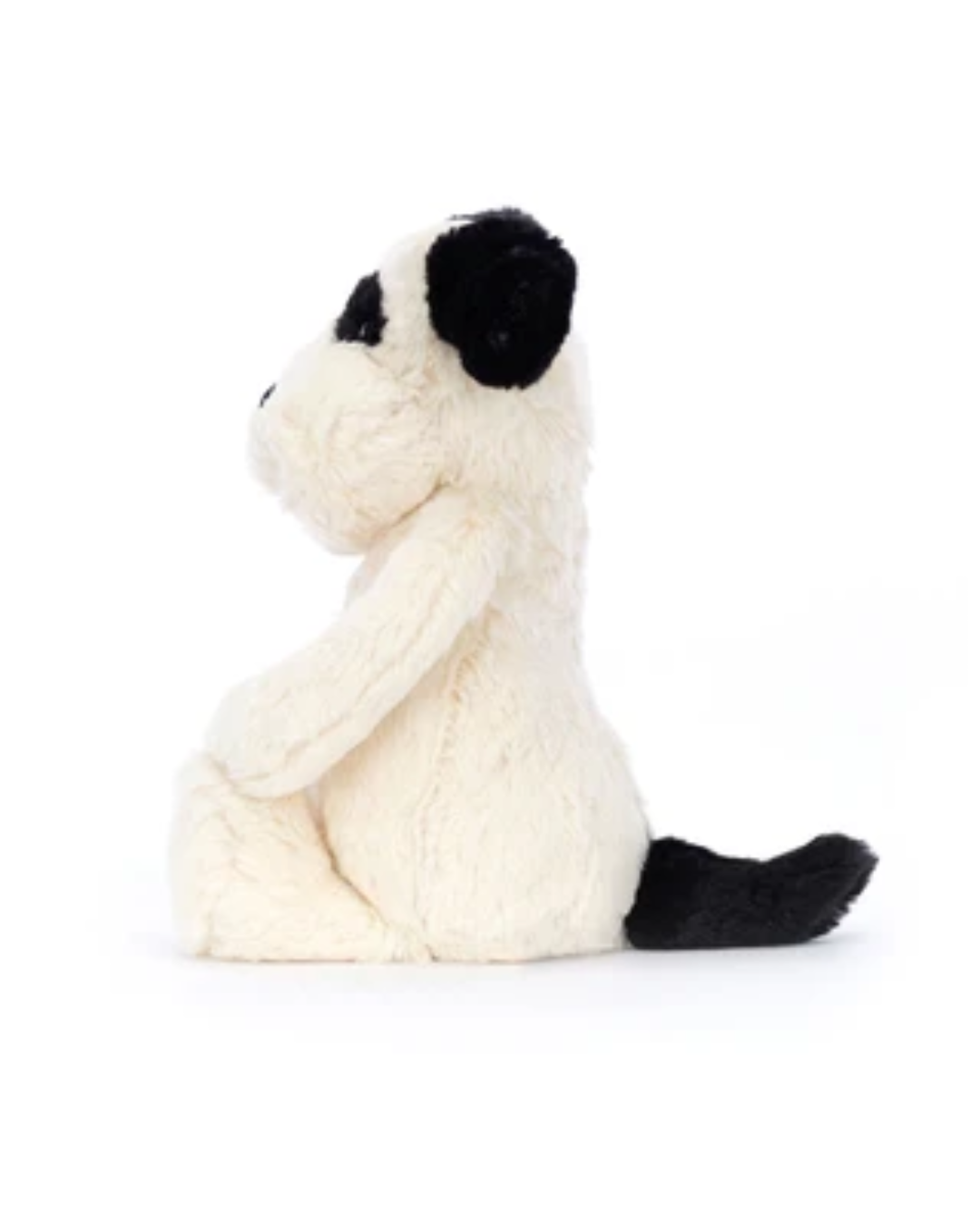 A plush puppy toy in a sitting position, featuring fluffy off-white fur with black patches on its ears, around the eyes, and on its tail, photographed against a seamless white background.