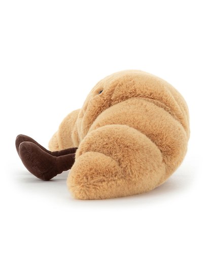 A plush croissant toy in a warm tan color with dark brown feet, photographed on a clean white background.