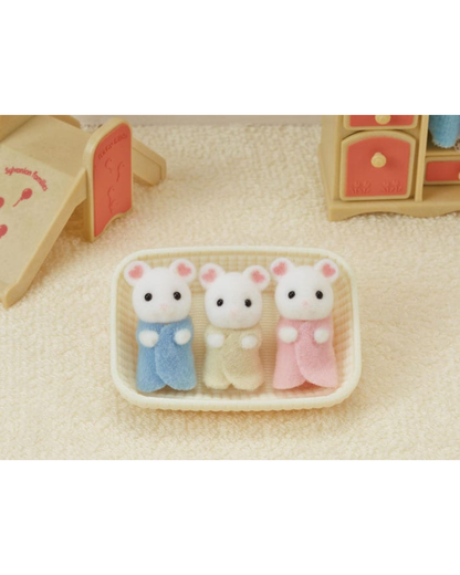 Three small Sylvanian Families marshmallow mice in pastel blue, cream, and pink outfits, arranged in a cream-colored basket on a textured beige surface.