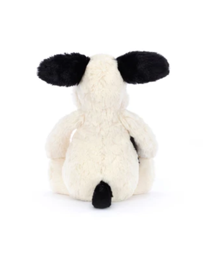 A plush puppy toy shown from the back, featuring fluffy cream-colored fur with black ears, a black tail, and a small black patch on its back, set against a plain white background.