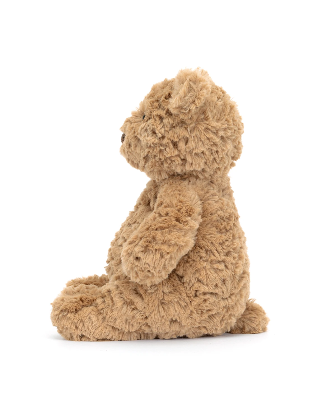 A plush teddy bear in a warm tan or light brown color, shown from the side sitting down on a clean white background.