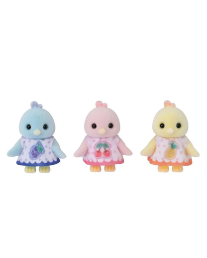 Three Sylvanian baby bird figurines standing side by side on a plain white background. The left figure is light blue with a purple dress and fruit motif; the middle is pink with a pink dress and cherry motif; the right is pale yellow with an orange dress and pineapple motif.