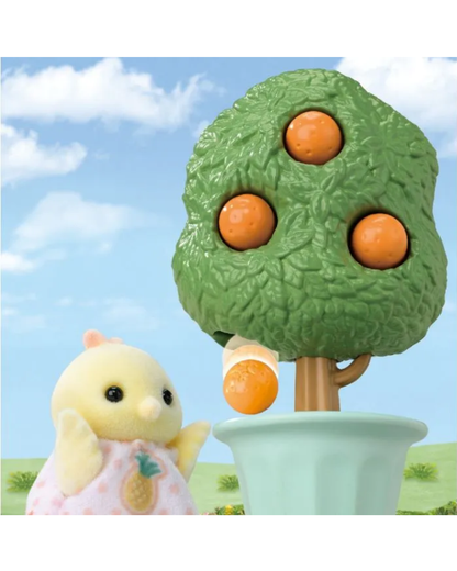 A small yellow Sylvanian chick in a pink dress stands beside a green fruit tree with three orange apples in a light blue pot against a blue sky background.
