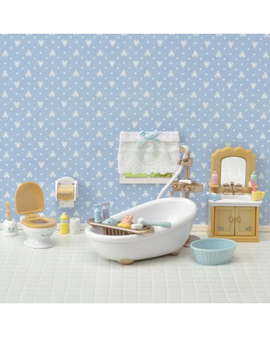 A Sylvanian toy bathroom set featuring a white bathtub with a wooden footrest, a small wooden vanity with a mirror, a toilet, and other matching accessories against a blue patterned wallpaper background.