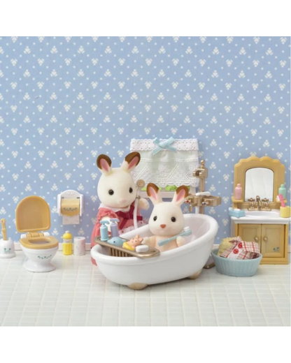 A Calico Bunny bath scene featuring two sylvanian bunny figurines in a white bathtub, surrounded by a miniature bathroom set with blue patterned wallpaper, a toilet, and a vanity cabinet.