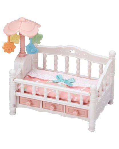 A small Sylvanian baby crib in white with pink bedding, a pink canopy, and hanging mobile accessories, shown on a plain white background.