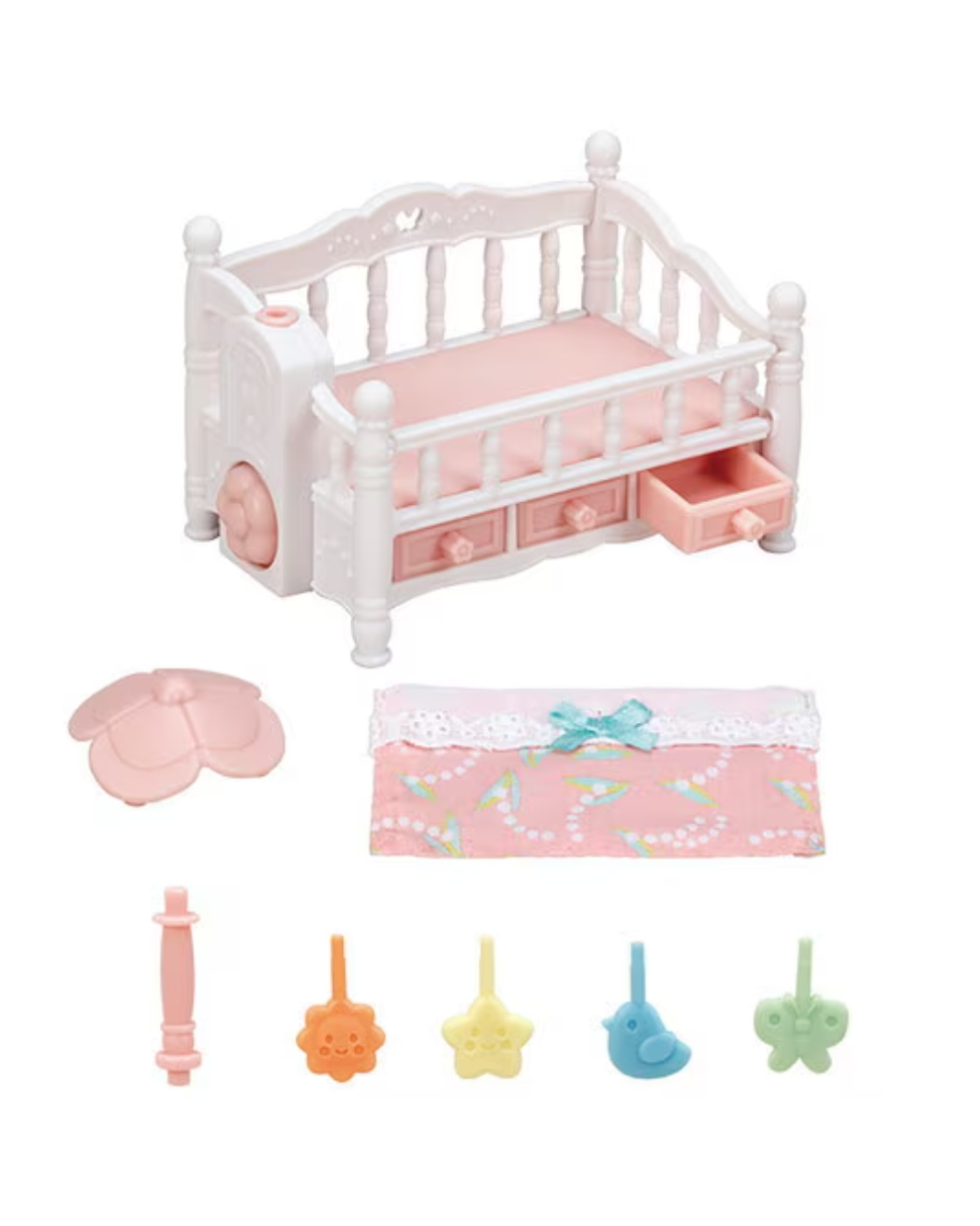 A small Sylvanian Families crib set in white and pink, shown with matching accessories including a pink flower-shaped item, a floral pouch with a blue bow, and four small star-shaped pieces in orange, yellow, blue, and green, all on a plain white background.