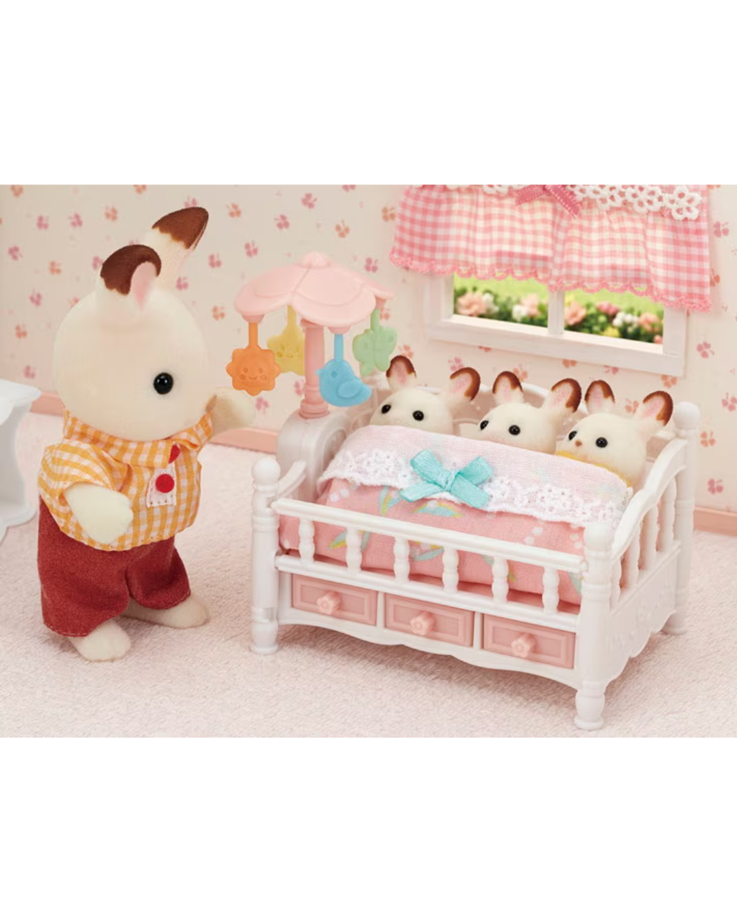 A Sylvanian family  scene featuring a rabbit family in a white crib with pink bedding and a mobile, alongside an adult rabbit figure in an orange-and-white check shirt and red pants in a pink patterned nursery.