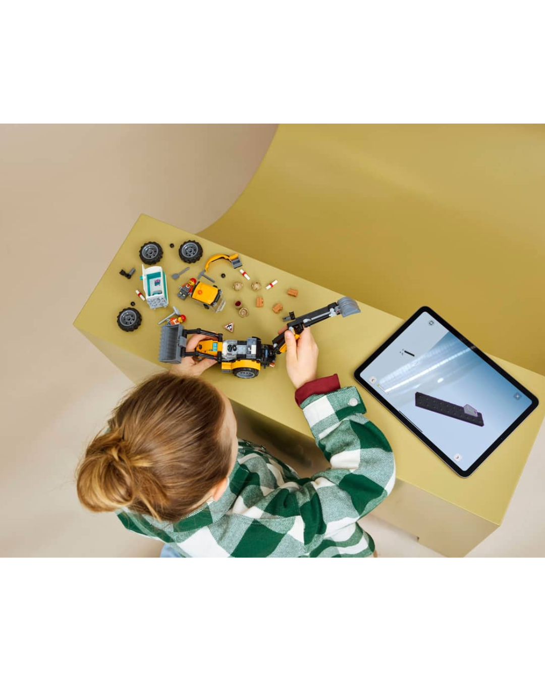 Child constructing LEGO 60480 Yellow Backhoe Loader V2  in front of yellow and brown background.