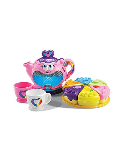 Leap Frog Musical Rainbow tea party set on a white background, featuring a smiling pink teapot with a blue mesh front, a pink cup, a white cup with a rainbow heart, and a round tray holding several brightly colored cupcake pieces.