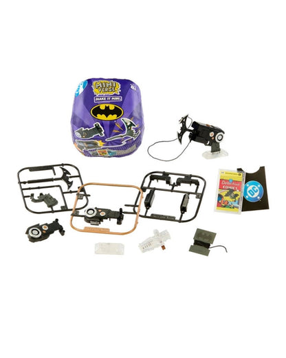A miniverse toy kit for children, featuring a purple Batman-themed miniverse capsule, various small plastic parts, two black motorized drone-like robots, a small instruction booklet, and a small accessory, all arranged on a plain white background.
