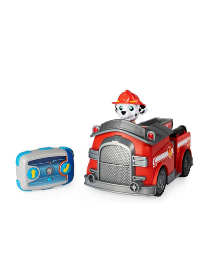 A Paw Patrol Marshall Fire Truck red toy fire truck with a dalmatian dog character sitting inside, shown alongside a blue and gray remote control on a plain white background.