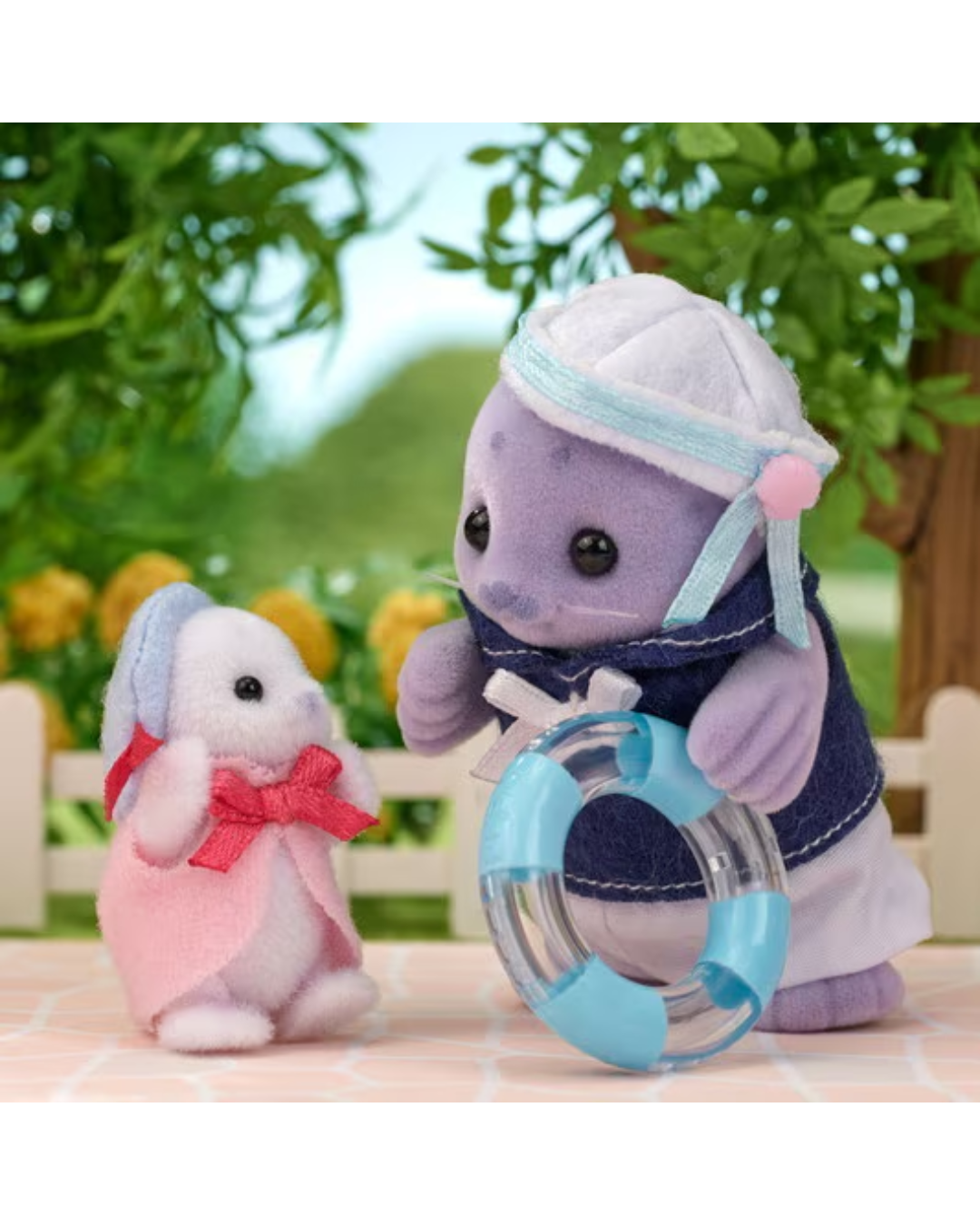 Sylvanian Families Seal father playing with baby seal. Both are wearing clothes and accessories and are standing in front of a blurred background with trees.