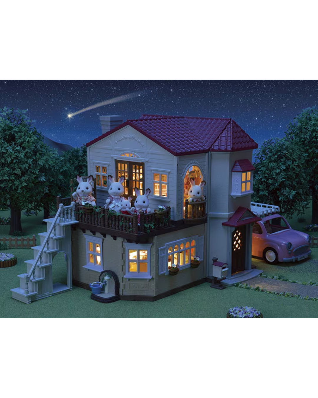 A Sylvanian Families model of a two-story house at night, featuring illuminated windows, a balcony with rabbit characters, an external staircase, a small car in a driveway, and a starry sky with a shooting star in the background.