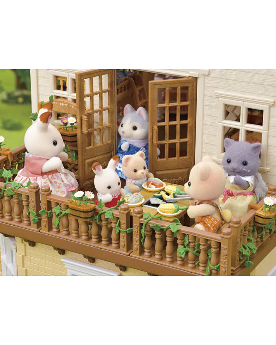 A Sylvanian Families miniature dollhouse scene showing several animal characters gathered on a balcony having a tea party. The house has cream-colored siding, brown wooden balcony railings and doors, and green ivy details.
