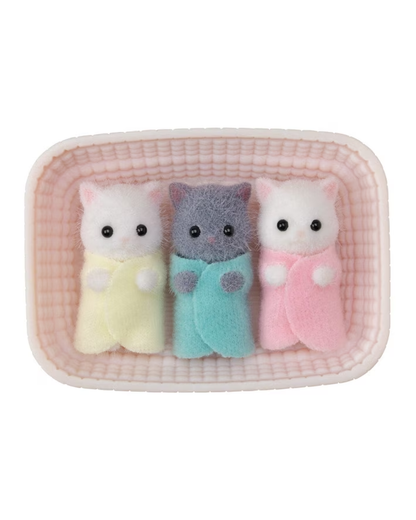 Three small plush cat figurines lying side by side inside a pink textured rectangular tray. The left cat is white with a pale yellow wrap, the middle cat is gray with a light blue wrap, and the right cat is white with a pink wrap.