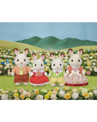 Four Sylvanian Family figurines dressed in colorful outfits, standing in a field of flowers with green hills and a blue sky backdrop.